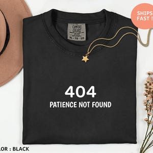 May include: Black t-shirt with the text "404 PATIENCE NOT FOUND" in white. A gold star pendant hangs from a delicate chain. The shirt is a size XL-TG-EG.