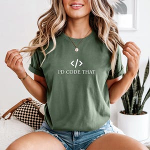 Könnte beinhalten: Olivgrünes T-Shirt mit dem weißen Text "I'D CODE THAT" und einem Code-Symbol. Das Shirt ist ein kurzärmeliges Rundhals-Modell.
