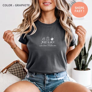 Puede incluir: Camiseta de color grafito con el texto "JUST A DEV who loves Halloween" y gráficos temáticos de Halloween. La camiseta es de color gris oscuro y tiene mangas cortas.