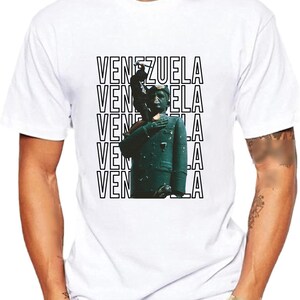 May include: White t-shirt with a black and white graphic print of a person in a green uniform with the word "VENEZUELA" repeated five times.