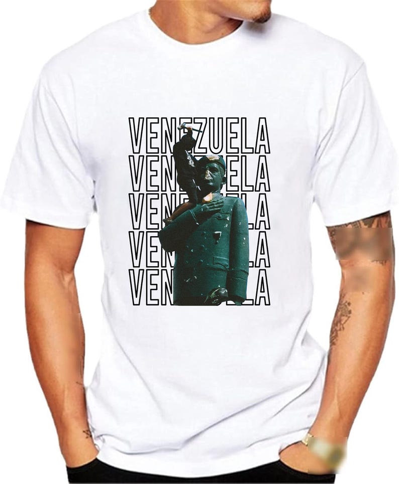 May include: White t-shirt with a black and white graphic print of a person in a green uniform with the word "VENEZUELA" repeated five times.