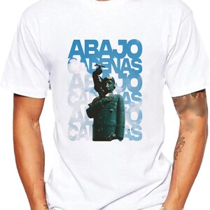 May include: White t-shirt with a blue and white graphic print of a person standing on a cloud with the text "ABAJO CADENAS" repeated multiple times.