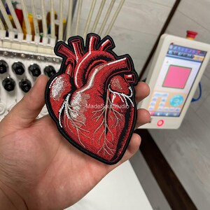 May include: Embroidered patch of a human heart in red and white, with black edging. The patch has the text "MadeSoulStudio". This patch is likely for clothing or accessories.