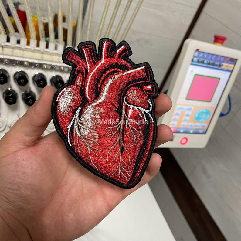 May include: Embroidered patch of a human heart in red and white, with black edging. The patch has the text "MadeSoulStudio". This patch is likely for clothing or accessories.