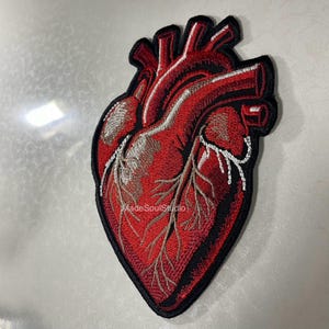 May include: Embroidered patch depicting a detailed anatomical heart in shades of red, with white and brown accents. The patch has a black border and the text "MadeSoulStudio".