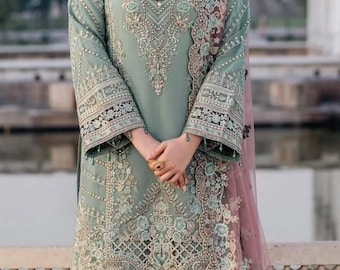 Puede incluir: Conjunto bordado verde mar, compuesto por una túnica de manga larga y pantalones a juego. El atuendo está adornado con intrincados patrones florales y geométricos, con una bufanda rosa transparente. Un collar de perlas y pendientes dorados completan el look.