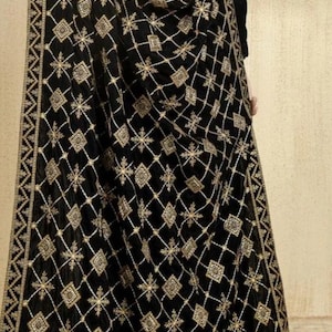 May include: Black shawl with an intricate gold embroidered geometric pattern. The design features diamonds, squares, and floral elements. The shawl's border has a detailed geometric design. This elegant accessory is suitable for formal occasions.