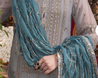 Puede incluir: Un vestido formal gris bordado con una bufanda verde azulado. El vestido presenta intrincados bordados dorados y una bufanda verde azulado a juego con detalles dorados. El atuendo es adecuado para ocasiones especiales.