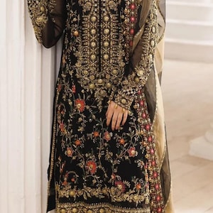 Può includere: Abito formale nero ricamato con motivi floreali dorati e rossi. L'abito presenta intricati abbellimenti dorati sul corpetto e sulle maniche, con una dupatta abbinata. L'outfit è in stile tradizionale.