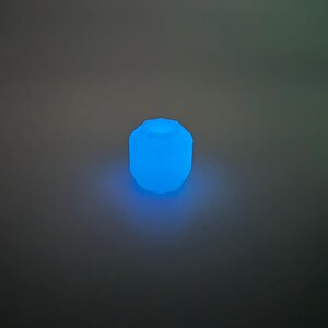 May include: A glowing, blue, geometric-shaped light fixture. The light emits a soft, ambient glow, creating a modern and inviting atmosphere. The fixture's design is simple yet eye-catching, perfect for adding a touch of color.