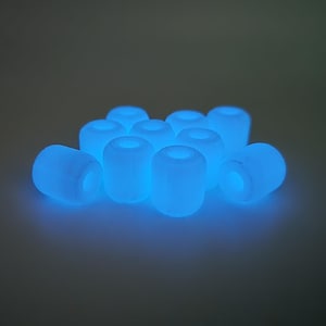 May include: A collection of glowing blue cylindrical beads. Each bead has a hole running through the center. The beads are scattered, creating a soft, ethereal glow.