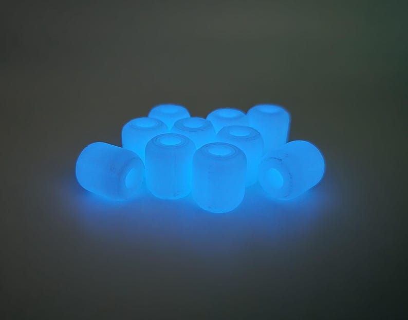May include: A collection of glowing blue cylindrical beads. Each bead has a hole running through the center. The beads are scattered, creating a soft, ethereal glow.