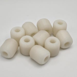 May include: A collection of off-white, cylindrical buoys with a central hole. These small, rounded objects are scattered against a plain white background. The buoys appear to be made of a smooth, solid material.