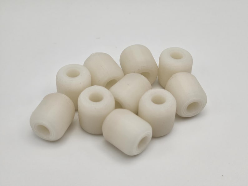 May include: A collection of off-white, cylindrical buoys with a central hole. These small, rounded objects are scattered against a plain white background. The buoys appear to be made of a smooth, solid material.