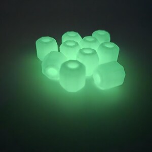 May include: A cluster of glowing, light green, cylindrical beads with a hollow center. The beads are arranged closely together, emitting a soft, ethereal glow against a dark background. The overall effect is a luminous, almost otherworldly appearance.