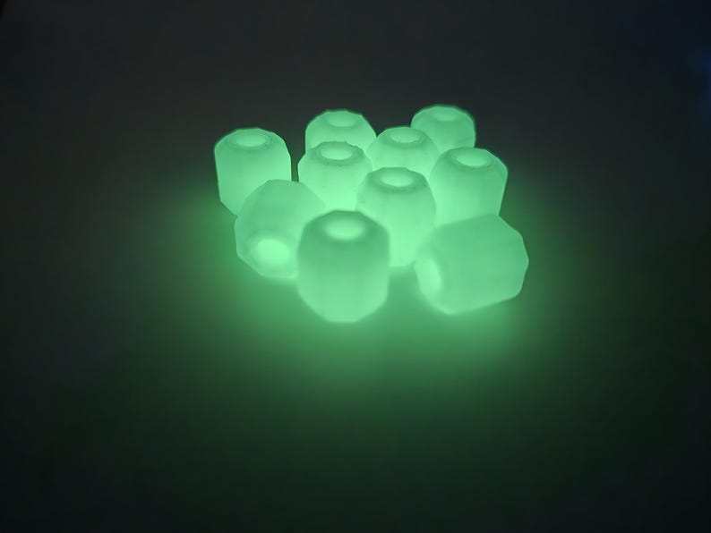 May include: A cluster of glowing, light green, cylindrical beads with a hollow center. The beads are arranged closely together, emitting a soft, ethereal glow against a dark background. The overall effect is a luminous, almost otherworldly appearance.