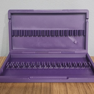 May include: A purple plastic storage case with two rows of slots for holding small items. The case is open and the slots are visible.