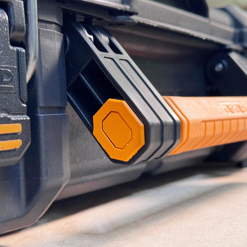 Peut inclure: Gros plan sur une poign&eacute;e de bo&icirc;te &agrave; outils noire et orange. La poign&eacute;e est orange avec une prise textur&eacute;e et des accents noirs. Le m&eacute;canisme de verrouillage est noir avec un bouton octogonal orange. La bo&icirc;te &agrave; outils est noire.