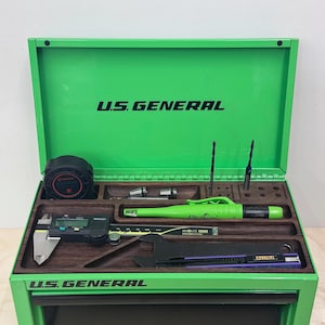 Könnte beinhalten: Ein hellgrüner U.S. General Werkzeugkasten mit offenem Deckel und einem dunklen Holzeinsatz. Das Fach enthält ein schwarzes Maßband, einen digitalen Messschieber, einen grünen Druckbleistift, zwei Bohrer, einen schwarzen Schraubenschlüssel und ein Cuttermesser.