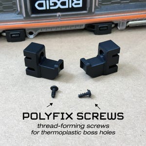 May include: Two black Polyfix screws and two black plastic brackets are displayed on a light brown surface. The text "POLYFIX SCREWS" and "thread-forming screws for thermoplastic boss holes" are also visible.