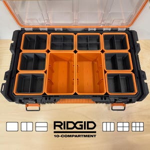 Puede incluir: Un organizador de herramientas Ridgid negro y naranja de 10 compartimentos con tapa transparente. El organizador tiene m&uacute;ltiples compartimentos de varios tama&ntilde;os, con interior naranja y negro. El logotipo de Ridgid y el texto "10-compartimentos" son visibles.