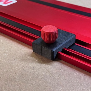 May include: A red aluminum track with a black rubber strip and a black sliding block featuring a textured red circular knob. The block is positioned on the track, which has a smooth metallic finish and a visible white letter W in the corner.