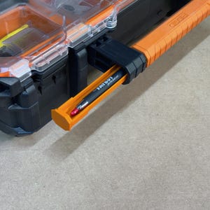 Peut inclure: Organisateur d'outils noir et orange avec un couvercle transparent. Un stylo noir avec le texte "FATBOY per the read out" est dans un support orange. La poign&eacute;e de l'organisateur d'outils est orange et noire.