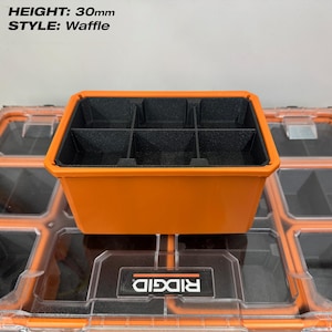 May include: An orange storage container with six black compartments. The container is labeled "STYLE: Waffle" and has a height of 30mm. The container is sitting on top of a clear storage container with an orange frame.