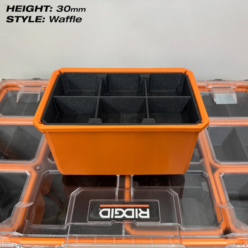 May include: An orange storage container with six black compartments. The container is labeled "STYLE: Waffle" and has a height of 30mm. The container is sitting on top of a clear storage container with an orange frame.