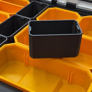 Peut inclure: Un bac de rangement rectangulaire en plastique noir inséré dans une mallette plus grande dotée de compartiments jaune vif. Le bac noir présente une finition mate lisse avec de petites languettes verticales sur les bords supérieurs.