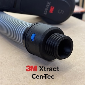 Puede incluir: Primer plano de un accesorio de manguera de aspiradora 3M Xtract Cen-Tec negro y gris. El accesorio tiene un botón azul y una manguera gris flexible y acanalada. Los logotipos 3M Xtract y Cen-Tec son visibles en rojo y negro.