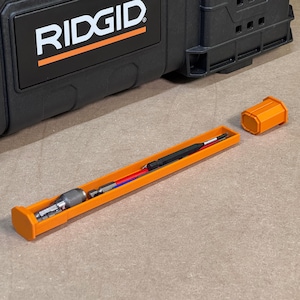 Op de afbeelding: Een open oranje gereedschapskist met de merknaam "RIDGID" in witte letters. Binnenin bevindt zich een set gereedschappen, waaronder een schroevendraaier en bits. De gereedschappen zijn netjes gerangschikt in een oranje bak.