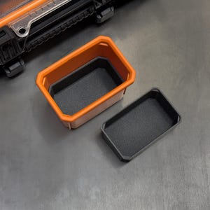 May include: An orange and black rectangular storage container with a removable tray. The container has a textured interior and exterior. The tray is black and has a textured surface. The container is open and empty.