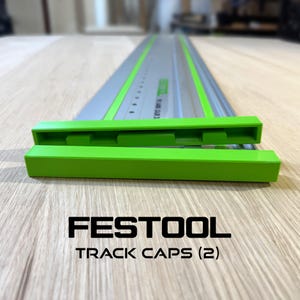 Könnte beinhalten: Ein Satz grüner Führungskappen für eine Festool Führungsschiene, mit Markennamen und Produktbeschreibung in schwarzer Schrift. Die Kappen passen auf eine grau-grüne Schiene und ermöglichen präzise Schnitte bei Holzbearbeitungsprojekten.