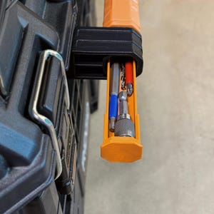 Peut inclure: Gros plan sur une bo&icirc;te &agrave; outils noire et orange avec un compartiment orange coulissant. Le compartiment contient divers forets et embouts de tournevis. La bo&icirc;te &agrave; outils a un loquet en m&eacute;tal argent&eacute;.