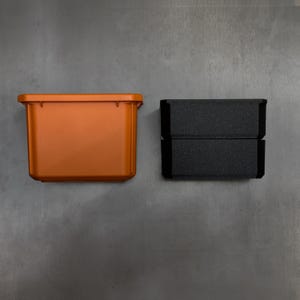May include: An orange plastic container and a black foam insert. The container has a rectangular shape and a lip around the top edge. The foam insert is made of two stacked pieces. The container is likely used for storage.