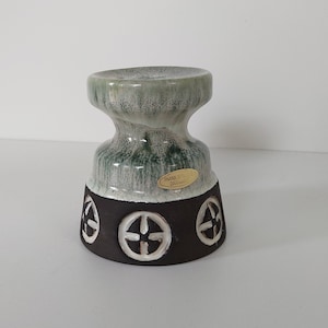 May include: A green and white ceramic candle holder with a brown base. The base has a design of four white circles with a cross in the center. The candle holder has a label that reads "Th. Trier, Germany".