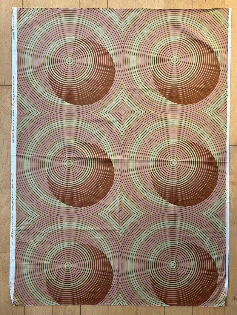 May include: A fabric with a repeating pattern of brown circles with concentric rings on a pink and green background.