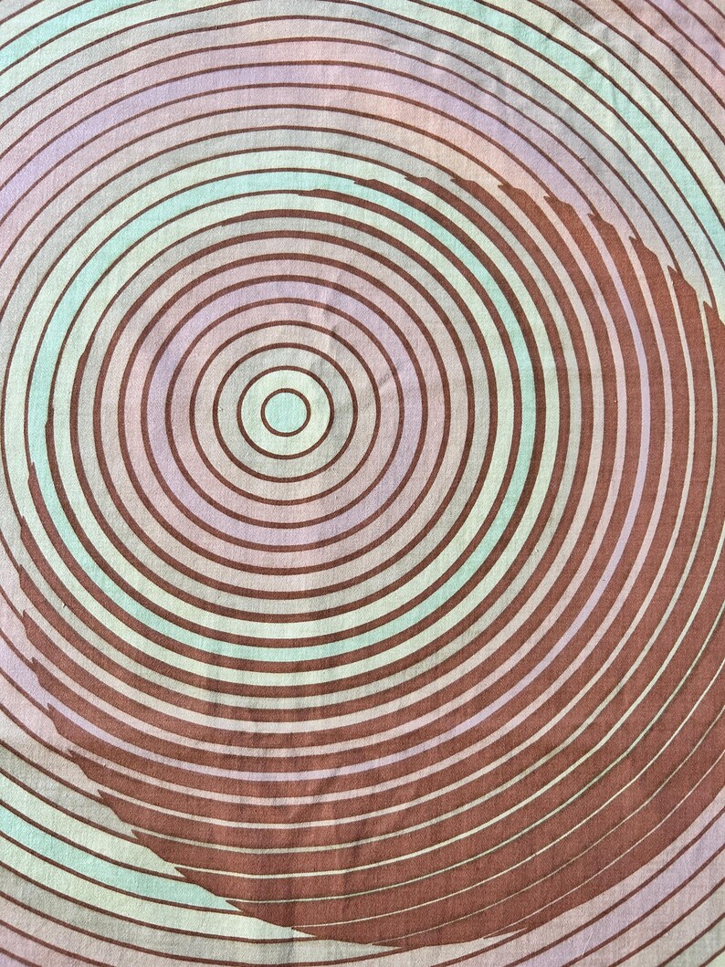May include: A close-up of a fabric with a circular pattern of concentric circles in shades of brown, pink, and blue.