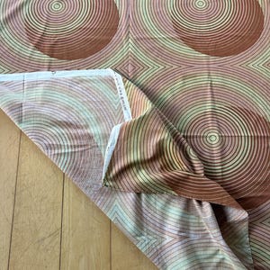 May include: A brown and pink fabric with a repeating pattern of concentric circles. The circles are in shades of brown, pink, and green.