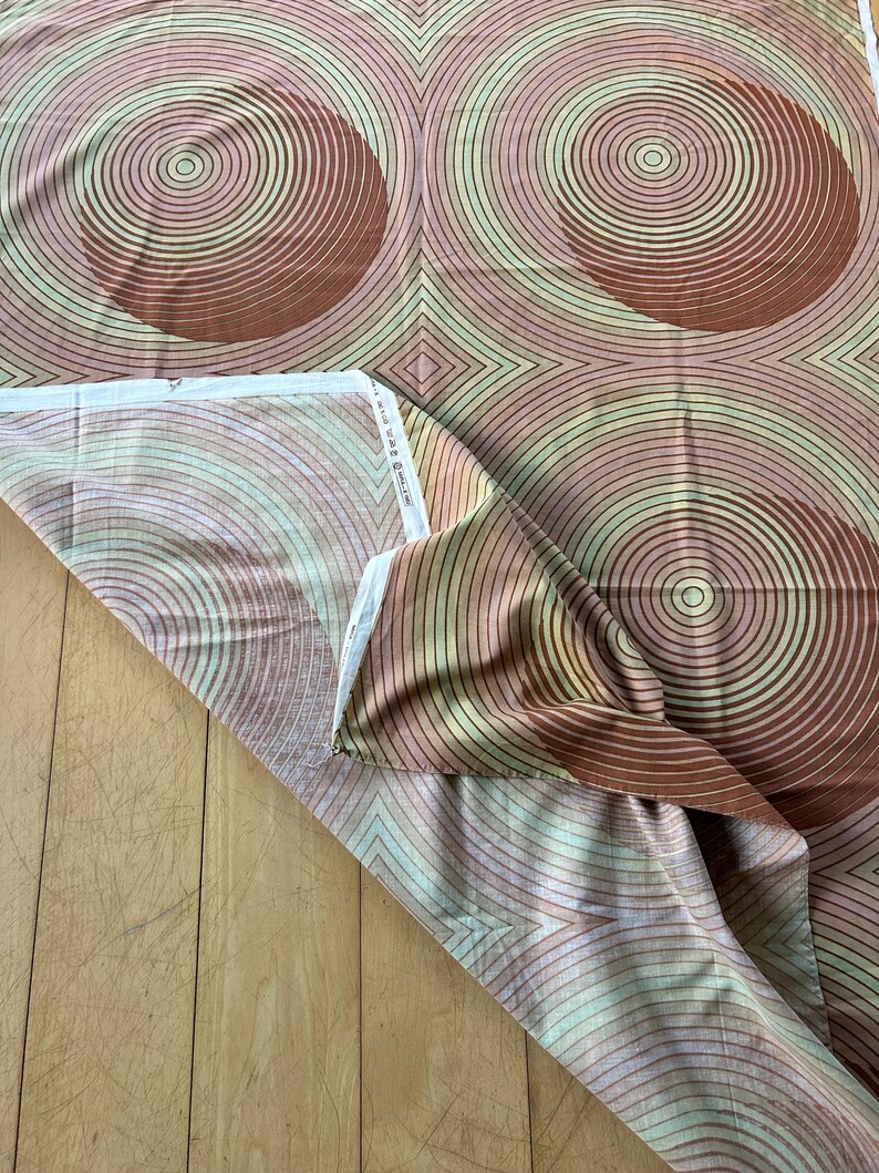 May include: A brown and pink fabric with a repeating pattern of concentric circles. The circles are in shades of brown, pink, and green.