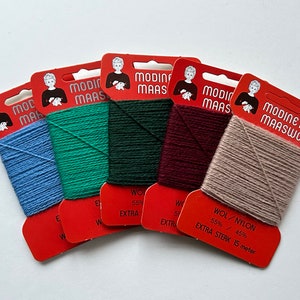 Op de afbeelding: Vijf spoelen garen in verschillende kleuren: lichtblauw, groen, donkergroen, bordeauxrood en beige. Het garen is gelabeld "Modinetje Maaswol" en "Extra Sterk 15 meter".