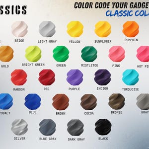 May include: A color chart displaying thirty-two small, spiraled, geometric objects in various shades. The text reads CLASSICS and COLOR CODE YOUR GADGETS WITH CLASSIC COLORS, followed by individual labels for each color including Jade White, Beige, Light Gray, Yellow, Sunflower, Pumpkin, Orange, Gold, Bright Green, Green, Mistletoe, Pink, Hot Pink, Magenta, Maroon, Red, Purple, Indigo, Turquoise, Cyan, Cobalt, Blue, Brown, Cocoa, Bronze, Gray, Silver, Blue Gray, Dark Gray, and Black.
