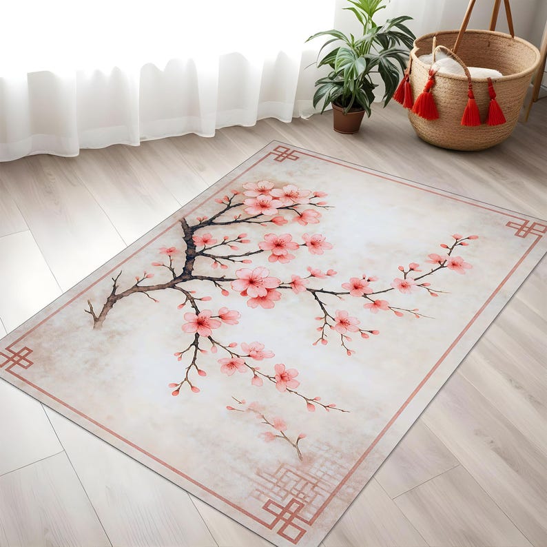 Op de afbeelding: Rechthoekig vloerkleed met een aquarelontwerp van een kersenbloesemtak met roze bloemen en bruine takken. Het vloerkleed heeft een lichtbeige achtergrond met een roze rand en decoratieve hoekelementen.