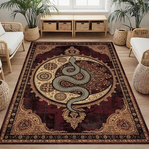Puede incluir: Una alfombra rectangular con un fondo burdeos y un diseño ornamentado. La alfombra presenta una gran serpiente estilizada enrollada alrededor de una luna creciente y intrincados patrones florales en oro y beige.