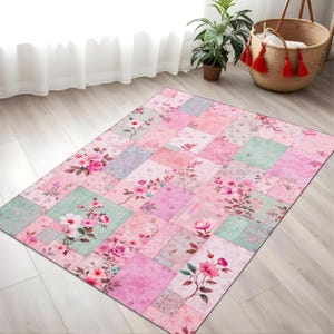 Op de afbeelding: Een roze en groene patchwork-kleed met bloemenmotieven. Het kleed is vierkant en gemaakt van een zacht, comfortabel materiaal.