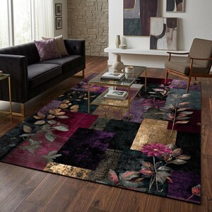 May include: A rectangular area rug featuring a patchwork design of deep purple, black, and gold metallic-toned blocks. The rug is decorated with large, detailed botanical illustrations of dark green leaves and vibrant magenta flowers.