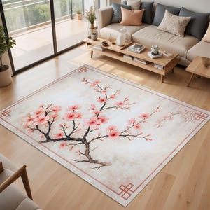 Op de afbeelding: Rechthoekig vloerkleed met een bloemenontwerp. Het vloerkleed heeft een aquarelachtige weergave van een kersenboom met roze bloemen en bruine takken. Het vloerkleed heeft een lichtbeige achtergrond en een roze rand.