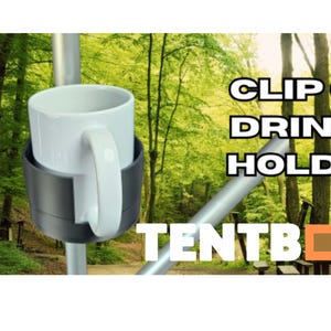 Puede incluir: Una taza blanca se encuentra en un portavasos negro con clip, sujeto a un poste de metal. El soporte está etiquetado como "TENTBOX" y el texto "CLIP ON DRINKS HOLDER" se muestra en blanco. El fondo es una escena borrosa de un bosque.