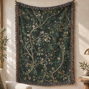 May include: A rectangular woven throw blanket featuring a dark forest green background with a repeating pattern of light brown tree branches, green leaves, and small white flowers, finished with a decorative multi-colored fringed edge.